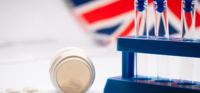 Laboratory test tubes and medicines in front of a UK flag, representing UK regulation of biomedical research and testing.