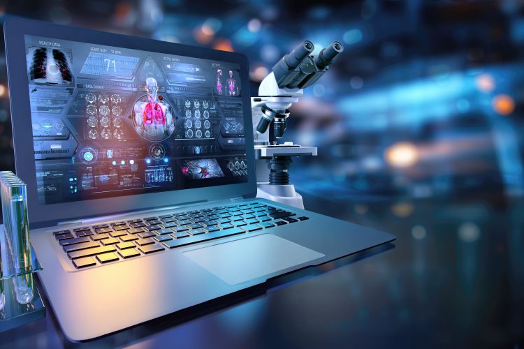 A laptop displaying a digital biomedical dashboard sits beside a laboratory microscope and test tubes, representing the integration of AI, data analysis, and laboratory research.