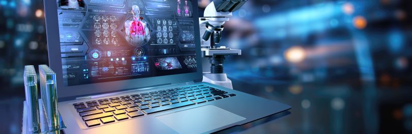 A laptop displaying digital health data and human anatomy visuals sits beside a microscope and test tubes in a modern laboratory, symbolizing the integration of real-world data, AI, and biomedical research in drug discovery.