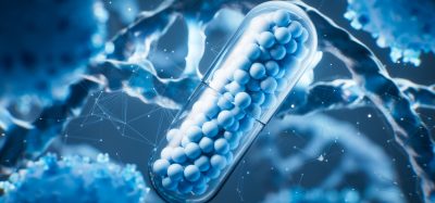 3D illustration of a pharmaceutical capsule filled with small blue spheres, surrounded by abstract biological cells and molecular structures, symbolizing drug discovery and biotechnology.