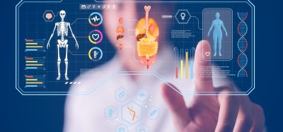 Doctor interacting with a futuristic digital medical interface showing human skeleton, organs, DNA strands, and health data visualisations, symbolising AI and precision medicine.