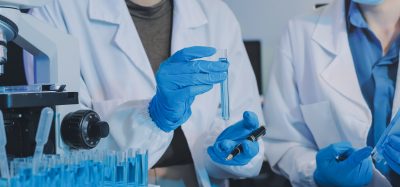 Scientists in a laboratory examining test tubes with blue liquid beside a microscope.