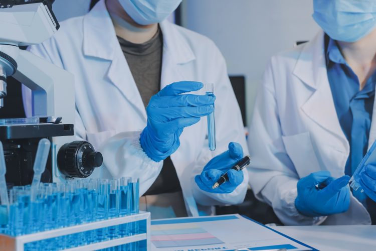 Scientists in a laboratory examining test tubes with blue liquid beside a microscope.