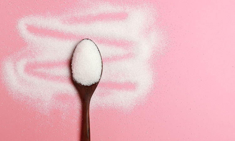 Sugar on spoon on pink background