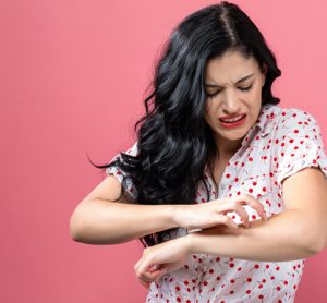 person scratching itchy arm on a pink background
