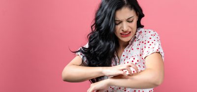 person scratching itchy arm on a pink background