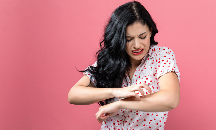 person scratching itchy arm on a pink background