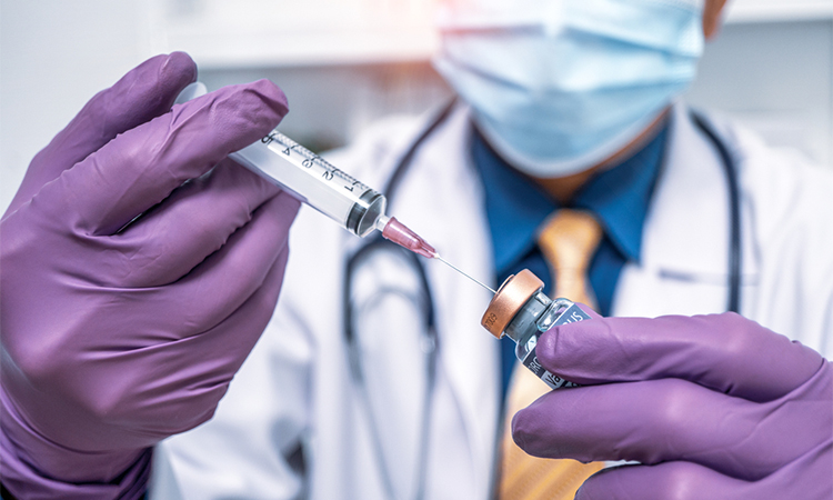 Close up doctor's hand in purple gloves holding vaccine bottle and needle